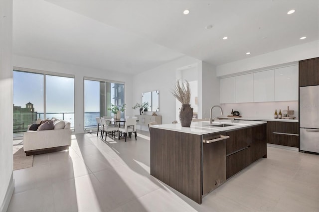 kitchen featuring sink, a water view, an island with sink, built in fridge, and white cabinets