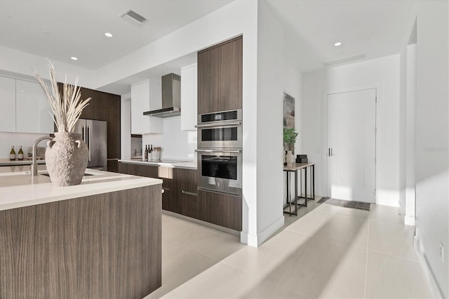 kitchen featuring white cabinetry, appliances with stainless steel finishes, wall chimney exhaust hood, and dark brown cabinets