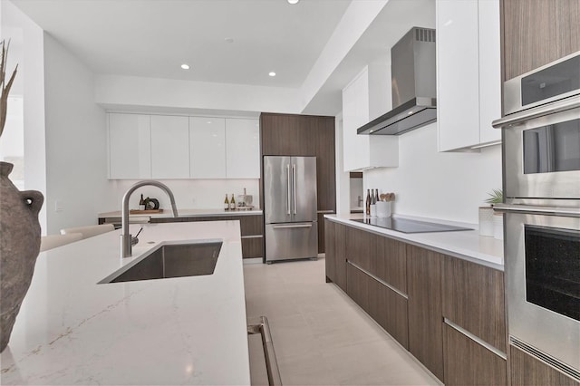 kitchen featuring sink, light stone counters, white cabinets, stainless steel appliances, and wall chimney range hood