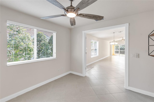 tiled spare room featuring ceiling fan with notable chandelier