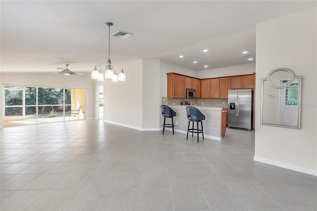 kitchen featuring light tile patterned floors, backsplash, stainless steel appliances, a kitchen breakfast bar, and decorative light fixtures