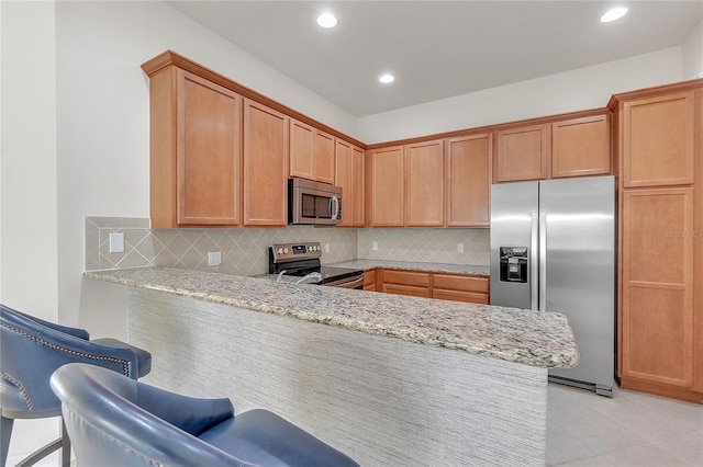 kitchen with light stone countertops, appliances with stainless steel finishes, a kitchen bar, and kitchen peninsula