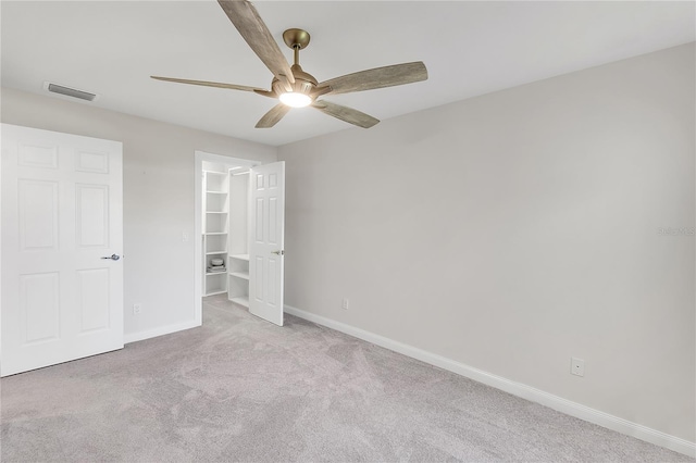 unfurnished bedroom featuring light carpet, a spacious closet, and ceiling fan