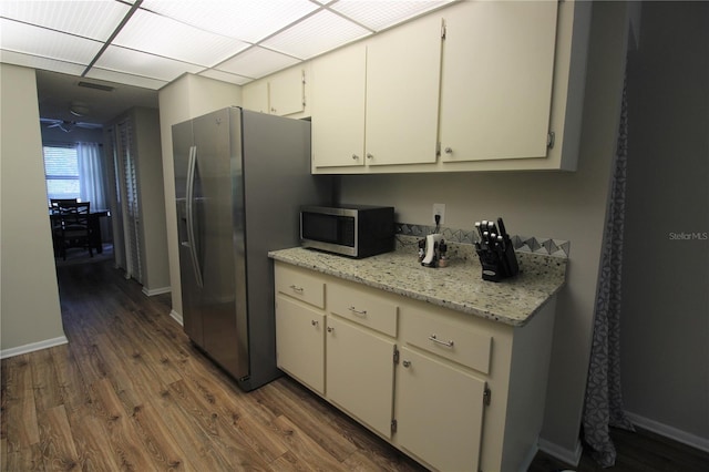 kitchen with dark wood-type flooring, white cabinetry, stainless steel appliances, light stone counters, and a drop ceiling