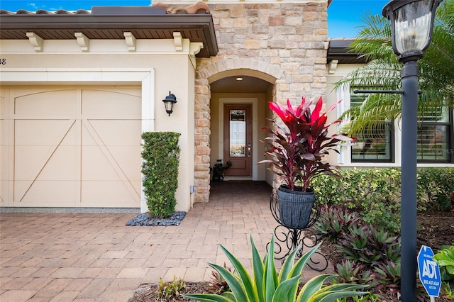 view of exterior entry featuring an attached garage, stone siding, and stucco siding