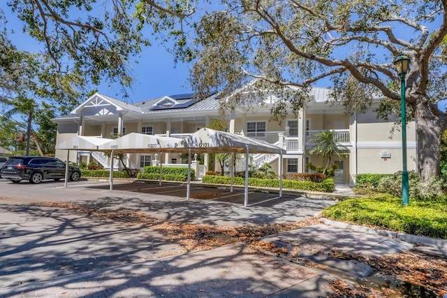 view of property featuring solar panels, stucco siding, metal roof, covered and uncovered parking, and a standing seam roof