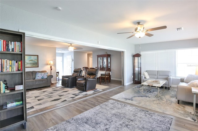 living area featuring a ceiling fan, plenty of natural light, visible vents, and wood finished floors