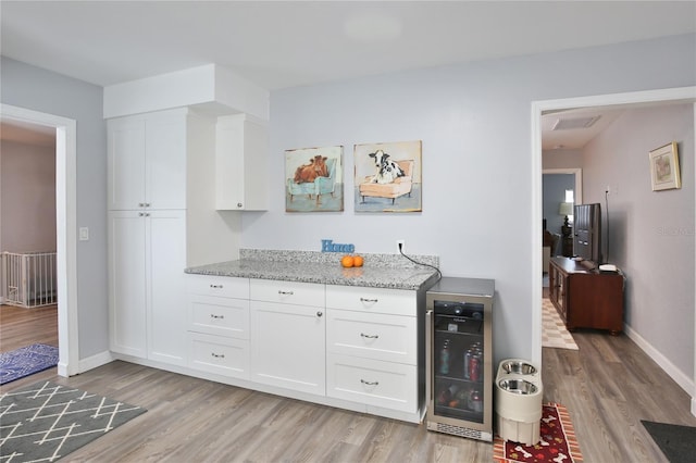 kitchen with beverage cooler, light stone counters, and light wood-style flooring