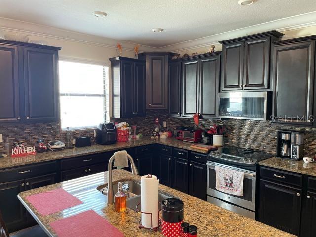 kitchen featuring tasteful backsplash, ornamental molding, appliances with stainless steel finishes, and sink