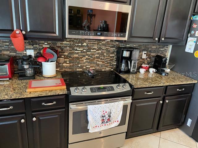 kitchen featuring light stone counters, backsplash, light tile patterned flooring, and appliances with stainless steel finishes