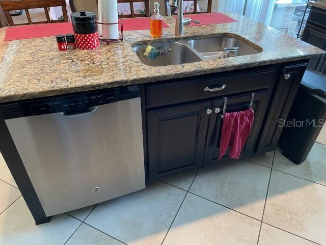 kitchen featuring light stone counters, sink, stainless steel dishwasher, and light tile patterned flooring