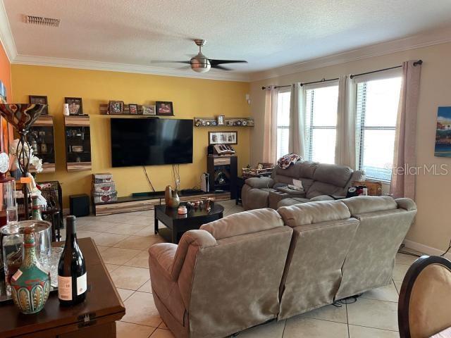 tiled living room with ceiling fan, ornamental molding, and a textured ceiling