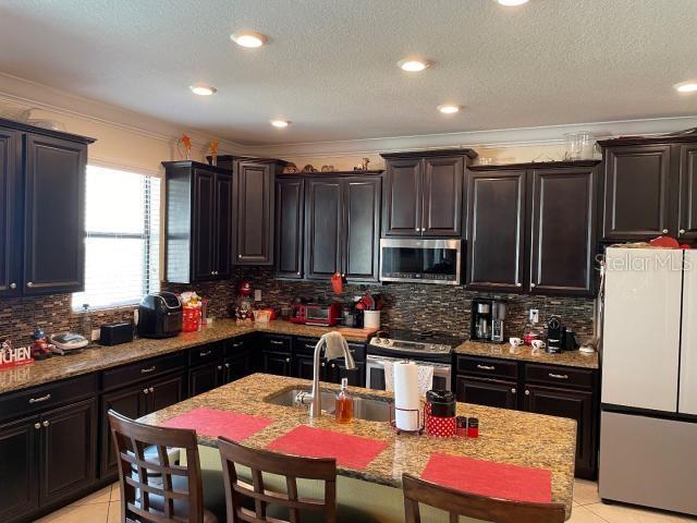 kitchen featuring light tile patterned flooring, sink, tasteful backsplash, stainless steel appliances, and light stone countertops