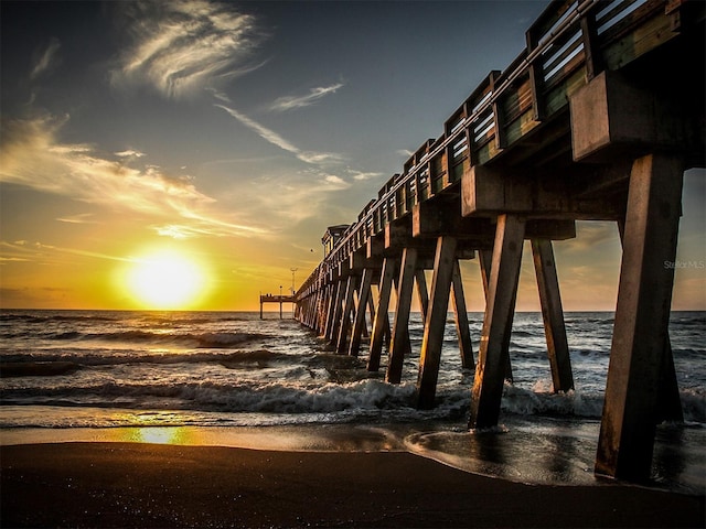 view of property's community featuring a pier, a water view, and a beach view