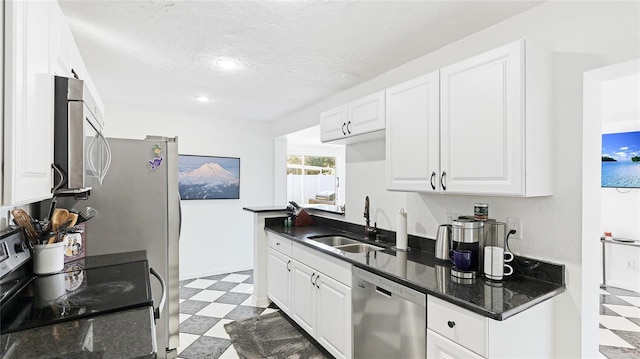 kitchen featuring appliances with stainless steel finishes, white cabinetry, sink, dark stone countertops, and a textured ceiling