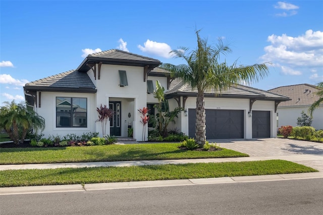 view of front of property featuring decorative driveway, stucco siding, an attached garage, a tiled roof, and a front lawn