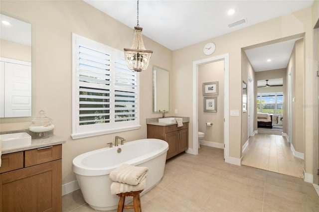 ensuite bathroom with a freestanding tub, toilet, connected bathroom, two vanities, and visible vents