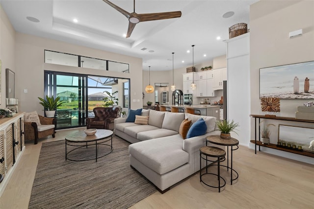 living room featuring light wood-style flooring, a raised ceiling, ceiling fan, and a towering ceiling