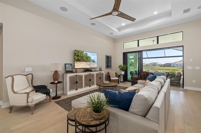 living area featuring light wood-type flooring, baseboards, visible vents, and a raised ceiling