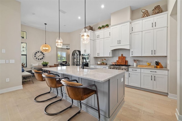 kitchen featuring a center island with sink, a breakfast bar, a sink, white cabinetry, and backsplash