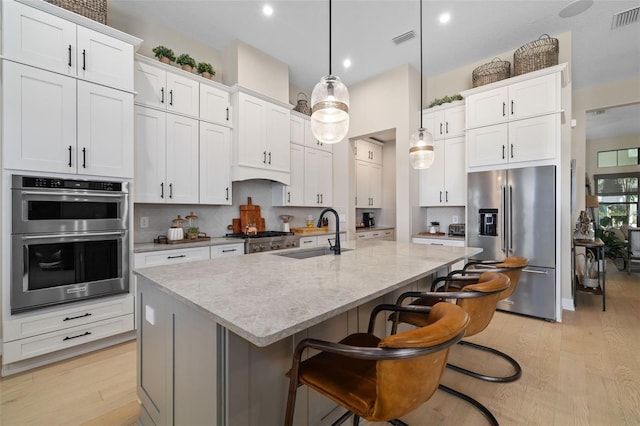 kitchen with light wood-style flooring, stainless steel appliances, a sink, visible vents, and a center island with sink