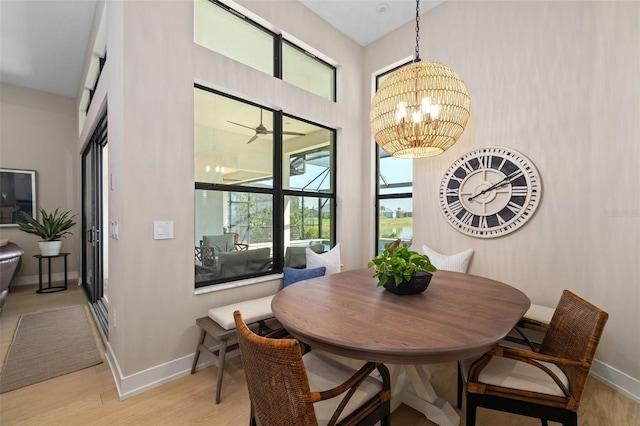 dining area with ceiling fan with notable chandelier, light wood-style flooring, and baseboards