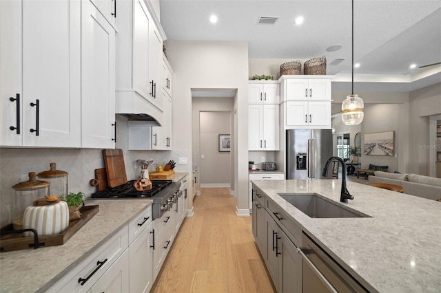 kitchen featuring light stone counters, visible vents, appliances with stainless steel finishes, a sink, and light wood-type flooring