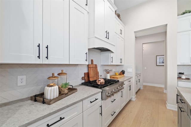 kitchen featuring light wood-style floors, white cabinets, decorative backsplash, light stone countertops, and stainless steel gas stovetop