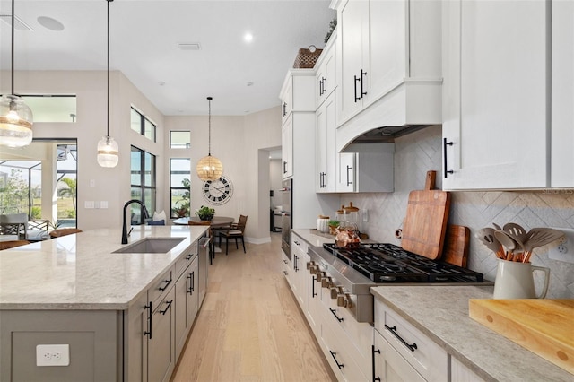 kitchen featuring light stone counters, a sink, light wood-style floors, appliances with stainless steel finishes, and an island with sink