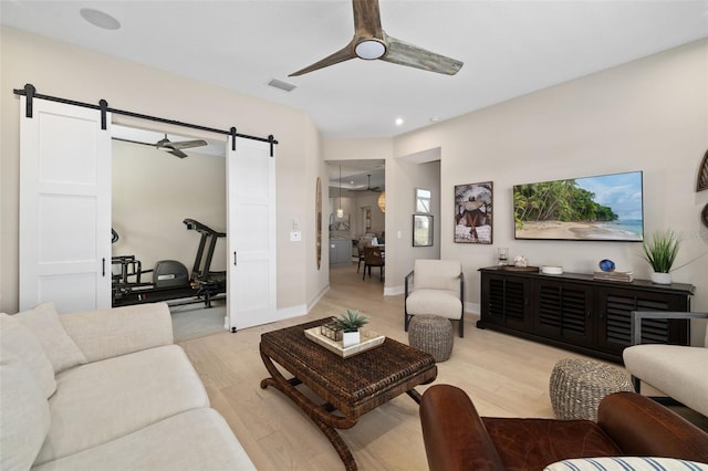 living room featuring a ceiling fan, visible vents, light wood finished floors, and a barn door