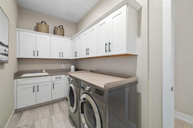 washroom featuring cabinet space, washing machine and dryer, baseboards, and a sink