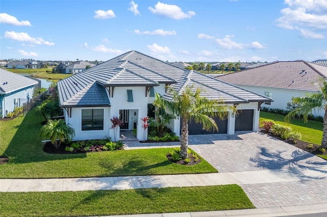 view of front of house featuring an attached garage, a tiled roof, decorative driveway, and a front yard