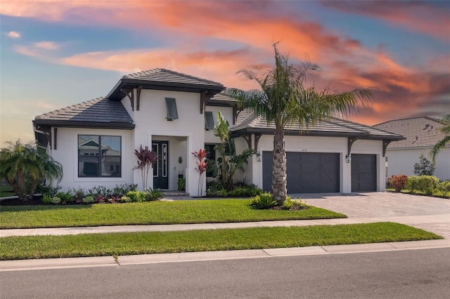 view of front of home with an attached garage, a tiled roof, decorative driveway, stucco siding, and a front lawn