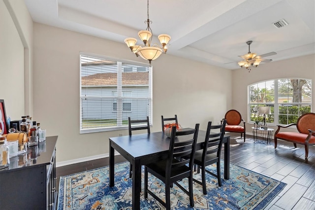 dining area featuring ceiling fan with notable chandelier, dark hardwood / wood-style floors, and a raised ceiling