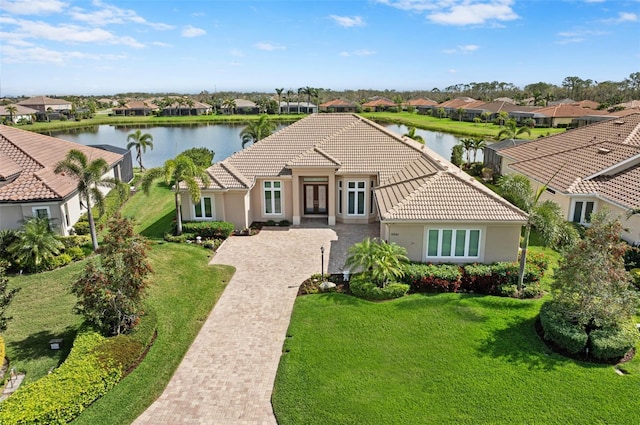 mediterranean / spanish home featuring a tile roof, a water view, a residential view, and a front lawn