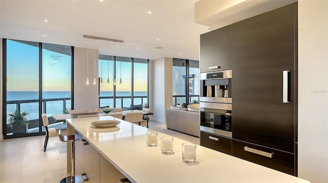 kitchen featuring floor to ceiling windows, a water view, light tile patterned floors, and stainless steel double oven