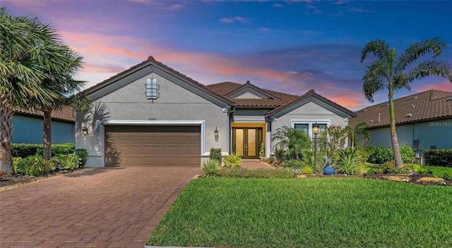 view of front of property featuring decorative driveway, an attached garage, stucco siding, a yard, and french doors