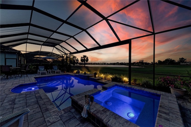 pool at dusk with a pool with connected hot tub, a water view, glass enclosure, and a patio area