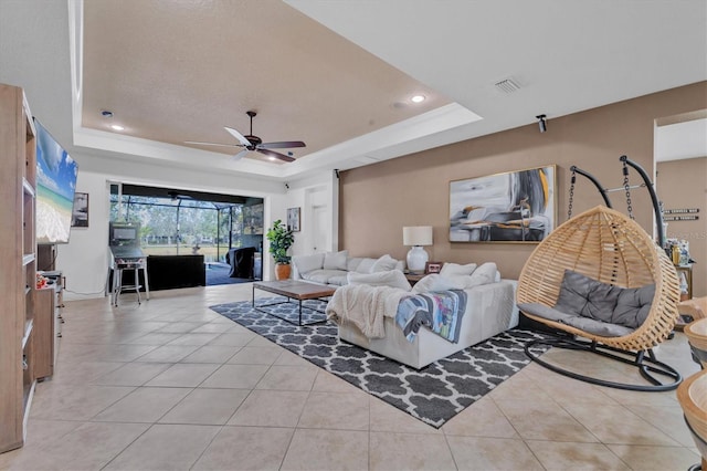 living room with ceiling fan, a raised ceiling, and light tile patterned floors