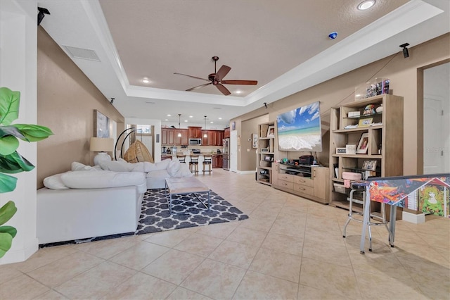 living room with light tile patterned floors, ornamental molding, a raised ceiling, and ceiling fan