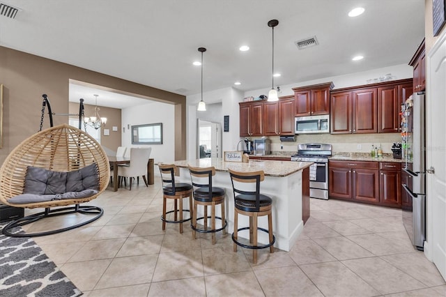 kitchen featuring appliances with stainless steel finishes, a kitchen bar, an island with sink, and hanging light fixtures