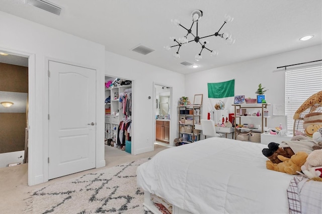 carpeted bedroom with ensuite bathroom, a walk in closet, an inviting chandelier, and a closet