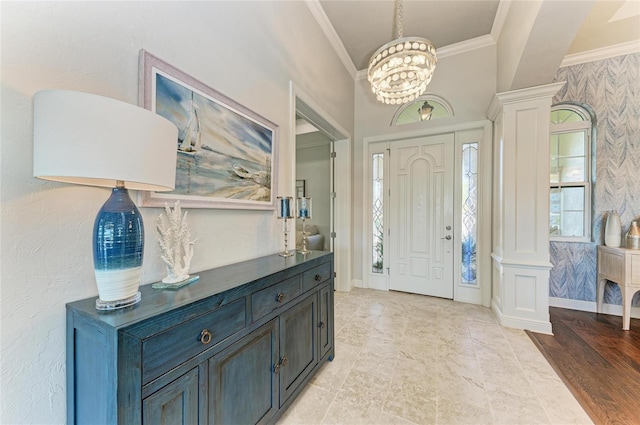 foyer entrance featuring decorative columns, crown molding, and a chandelier