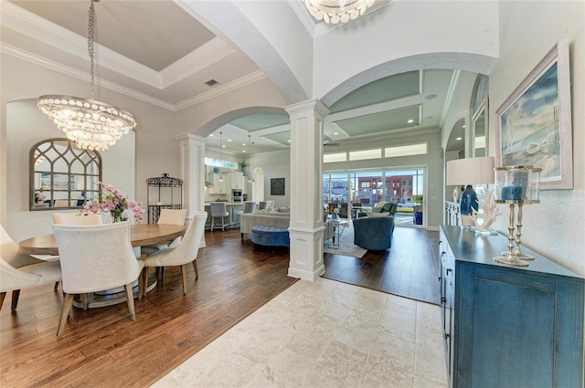 dining area with an inviting chandelier, crown molding, wood-type flooring, and decorative columns