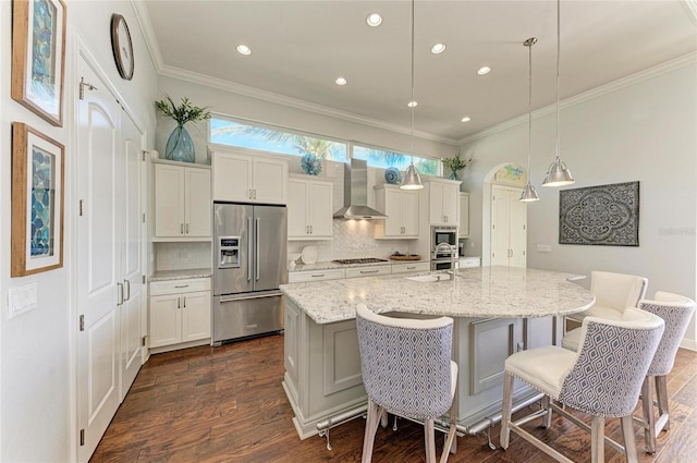 kitchen featuring a breakfast bar area, hanging light fixtures, a kitchen island with sink, stainless steel appliances, and wall chimney exhaust hood