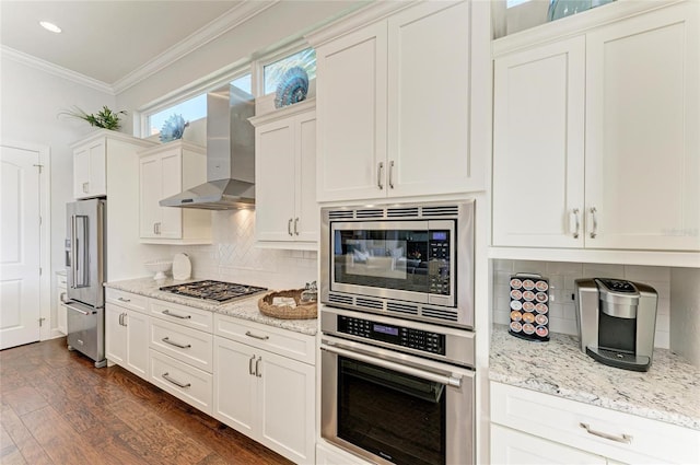 kitchen featuring light stone counters, wall chimney range hood, ornamental molding, stainless steel appliances, and white cabinets