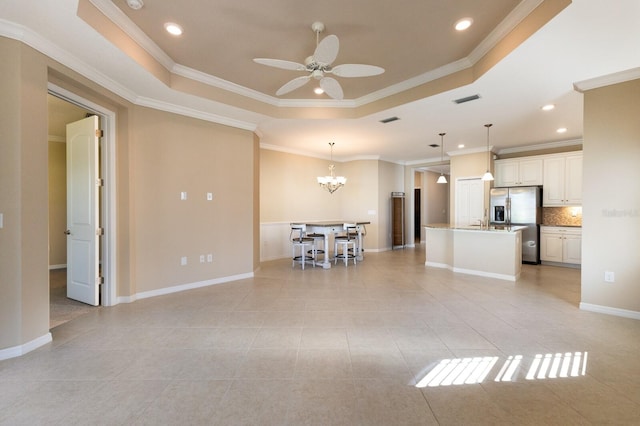 kitchen with stainless steel refrigerator with ice dispenser, tasteful backsplash, a raised ceiling, an island with sink, and pendant lighting