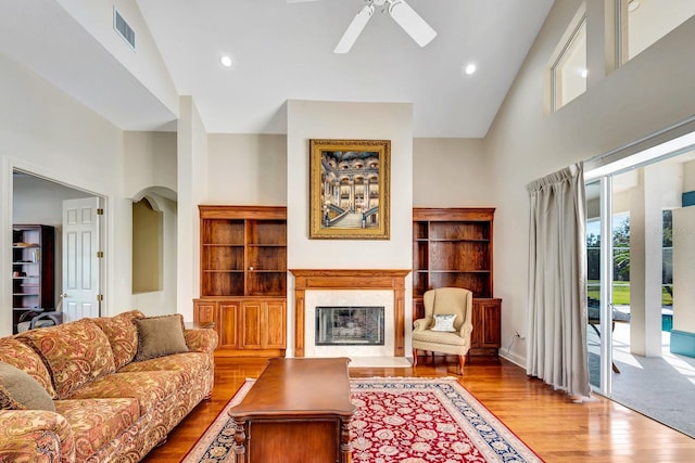 living room with ceiling fan, a premium fireplace, high vaulted ceiling, and light wood-type flooring