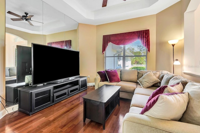 living room with dark wood-type flooring, a raised ceiling, and ceiling fan