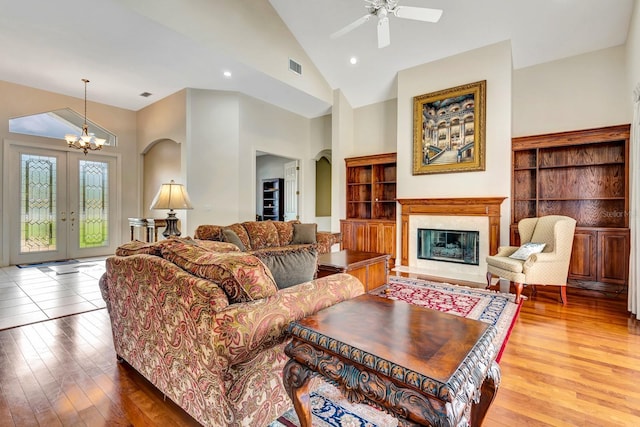 living room featuring hardwood / wood-style floors, ceiling fan with notable chandelier, a fireplace, and high vaulted ceiling